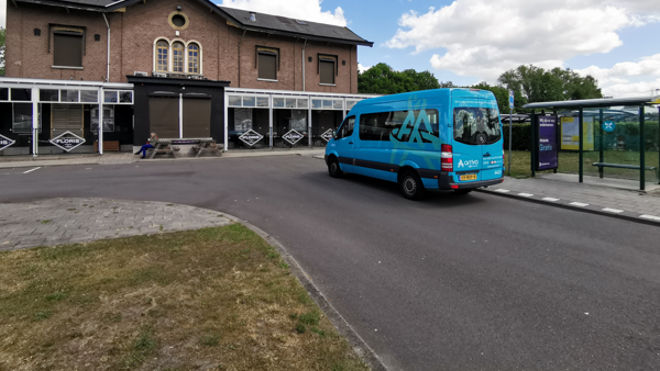 Kleine blauwe buurtbus staat geparkeerd bij een ouderwets, klein station.