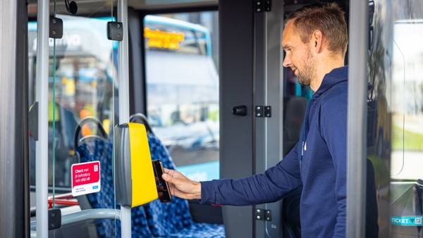 Man checkt met betaalpas op zijn telefoon in bij incheckpaal in bus van Arriva. Man checkt met betaalpas op zijn telefoon in bij incheckpaal in bus van Arriva.