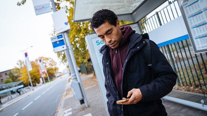 Een man staat bij een bushalte en kijkt op zijn telefoon.