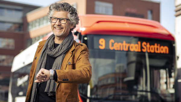 Man staat lachend op een station met een Arriva-bus met daarop '9 Centraal Station' achter hem.