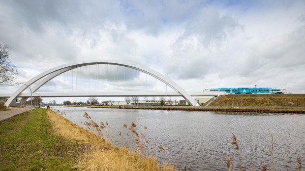 Een trein van Arriva rijdt richting een witte brug met hoge witte bogen. Een trein van Arriva rijdt richting een witte brug met hoge witte bogen.