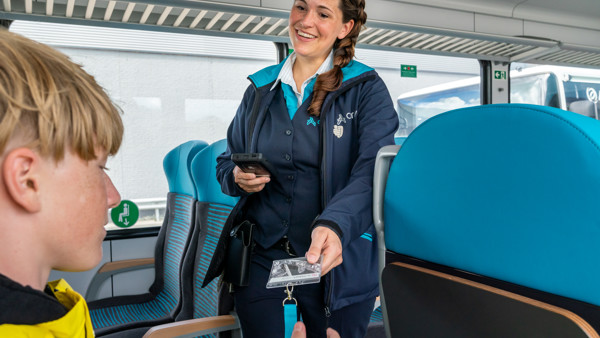Conductrice met vlecht in haar en in Arriva-uniform controleert de OV-chipkaart van een jonge reiziger.