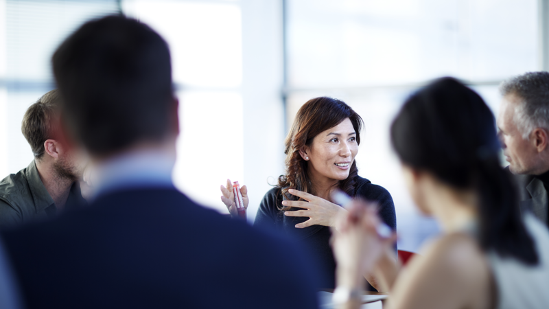 Een groep mannen en vrouwen in pakken zit om een tafel te vergaderen. Een groep mannen en vrouwen in pakken zit om een tafel te vergaderen.