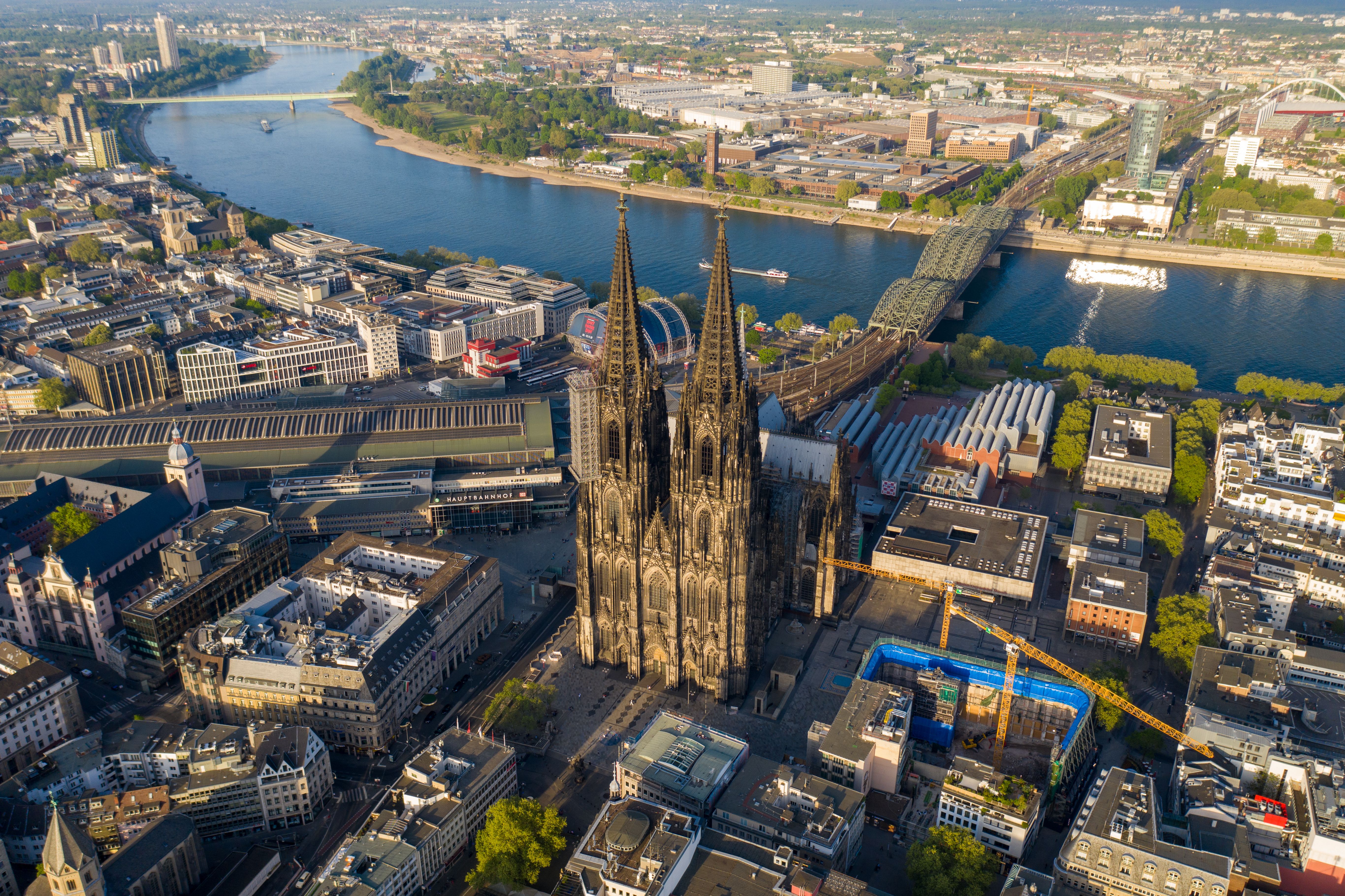 Keulen vanaf boven bekeken met de Dom op de voorgrond, de rest van de stad, een brede rivier met brug en nog meer stedelijk gebied daarachter.
