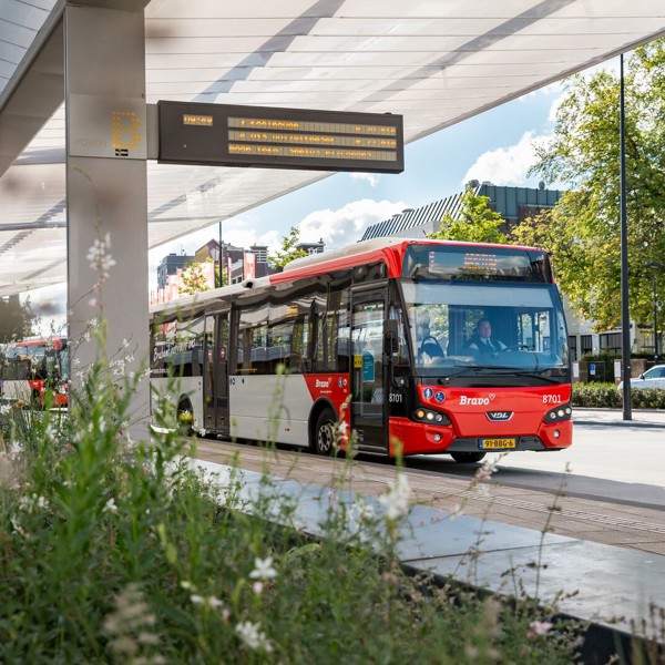 Een rode bus van Arriva staat bij een bushalte onder een overkapping op het voorplein bij treinstation Tilburg.