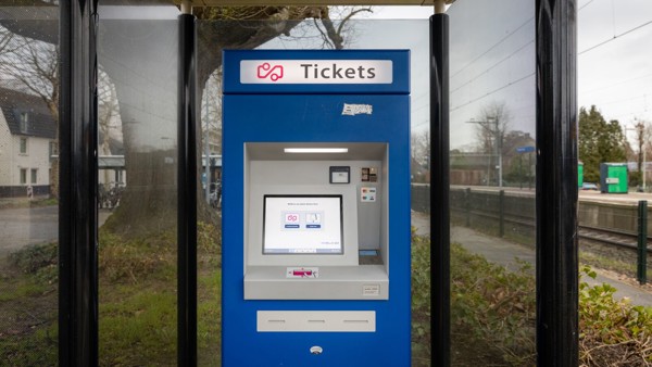 Blauwe ticketautomaat met touchscreen onder een overkapping op een treinperron.