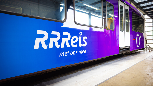 RRReis trein in Achterhoek en Rivierenland Bestickering van een RRReis trein in Achterhoek en Rivierenland, logo van RRReis met tekst: RRReis met ons mee. Trein in een werkplaats met blauwe en paarse huisstijlkleuren.