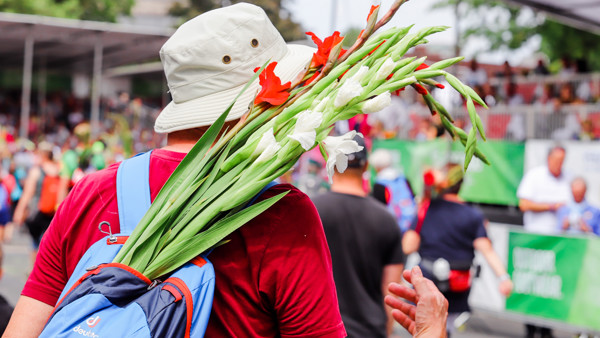 Witte en rode gladiolen steken uit blauwe rugzak van vrouw die meedoet aan de Nijmeegse Vierdaagse.
