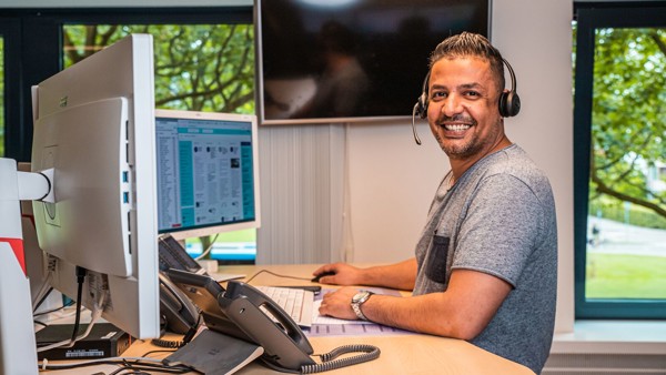 Medewerker achter bureau met headset lacht naar de camera.