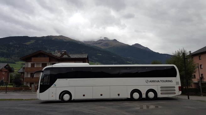 Een witte touringbus van Arriva rijdt door een bewolkt en bergachtig landschap.