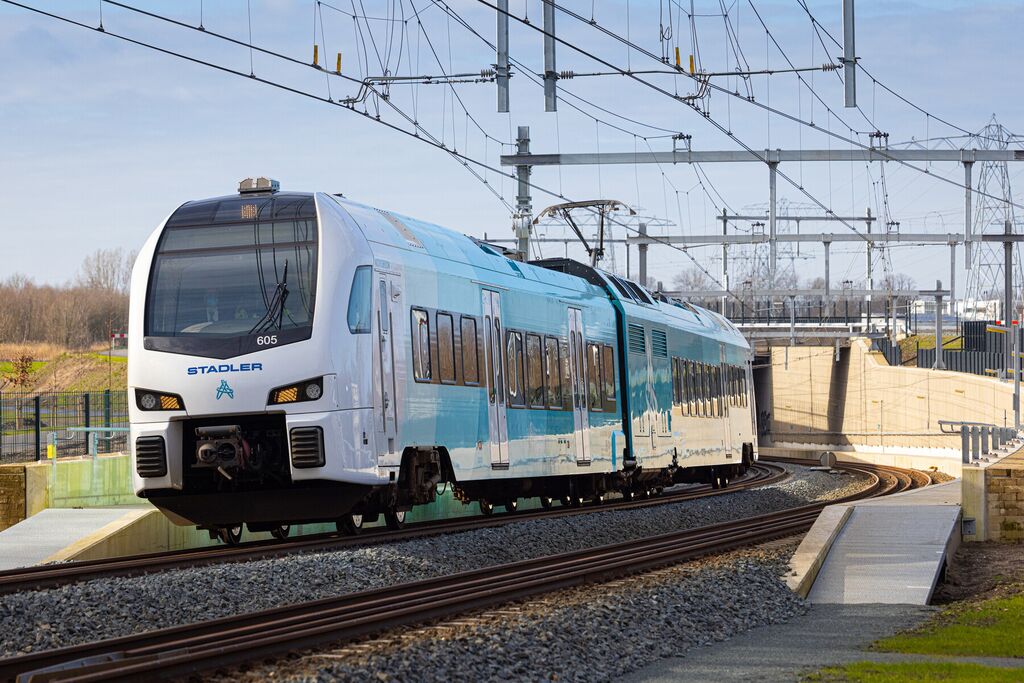 Een blauw-witte Arriva-trein rijdt over het spoor onder een blauwe lucht.