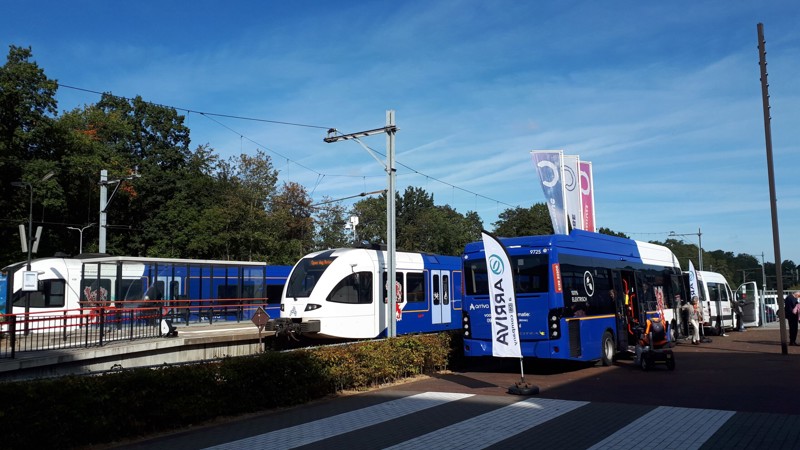 Twee blauwwitte treinen staan aan het perron met op de voorgrond een buurtbus van Arriva in dezelfde kleuren.