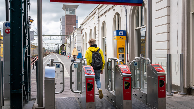 Jonge jongen in felgele jas vanaf de rug gezien is net door incheckpoortjes van Arriva gelopen en loopt het perron op.