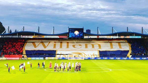 Het Willem II-stadion vanaf het veld bekeken richting het doel. Op de middenstip staan spelers, achter het doel hangt een grote Willem II-vlag over de tribune. Het Willem II-stadion vanaf het veld bekeken richting het doel. Op de middenstip staan spelers, achter het doel hangt een grote Willem II-vlag over de tribune.