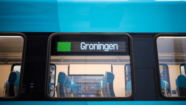Het zijraam van een lege, blauwe Arriva-trein met daarin de bestemming 'Groningen' weergegeven.