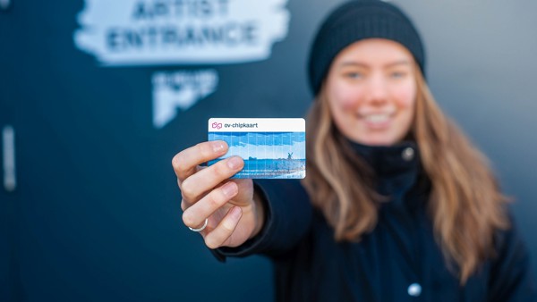 Vrouwelijke reiziger met muts en in winterkleding houdt een blauwe ov-chipkaart richting de camera.
