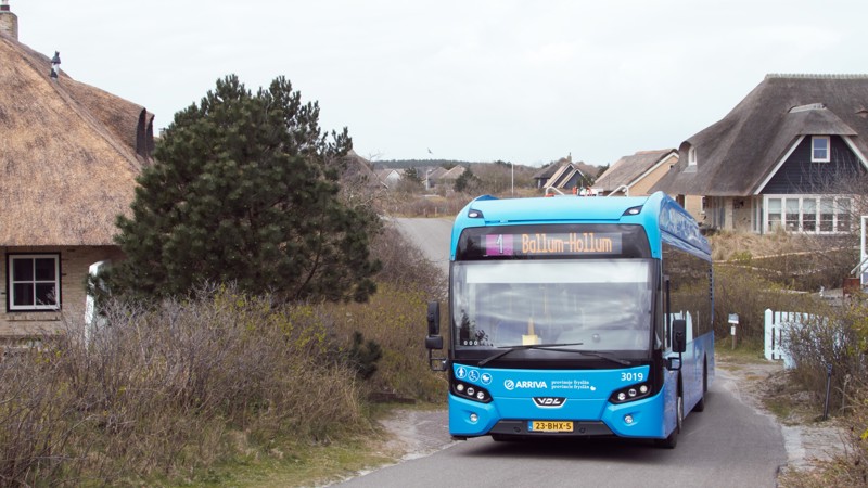 Een blauwe Arriva-bus rijdt door een straat met huizen, met de locatie Ballum-Hollum op de bus vermeld.