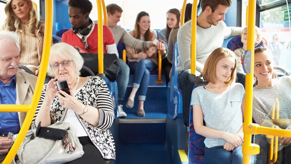 Achterste drie rijen stoelen in zonnige Arriva-bus, gevuld met diverse reizigers. Oud stel, man met klein kind, twee vriendinnen en een groepje vrienden creëren een positieve sfeer.