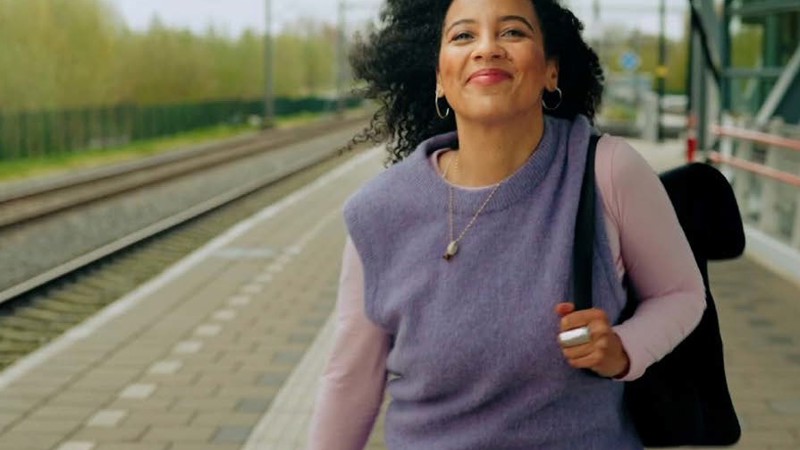 Vrouw met rugzak op staat lachend op een treinperron.