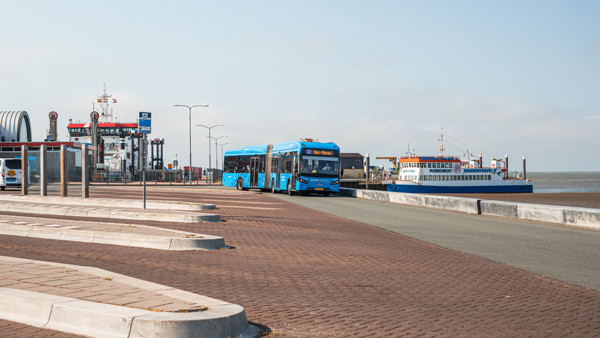 Blauwe bus van Arriva staat in de haven Ameland op de achtergrond zie je de veerboot.