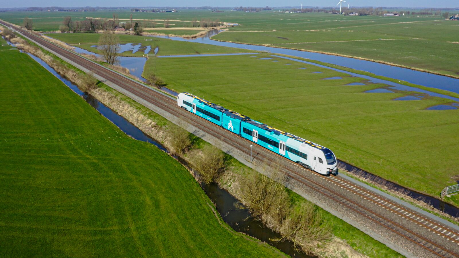 Blauwe trein van Arriva vanuit de lucht gezien terwijl hij in een groen weidelandschap rijdt.