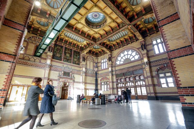 Het sierlijke en uitgebreid versierde plafond van de stationshal van station Groningen met daaronder reizigers.