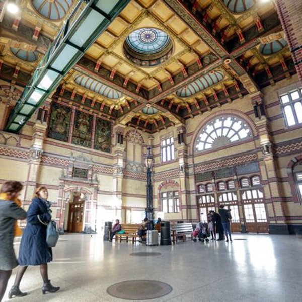 Het sierlijke en uitgebreid versierde plafond van de stationshal van station Groningen met daaronder reizigers.