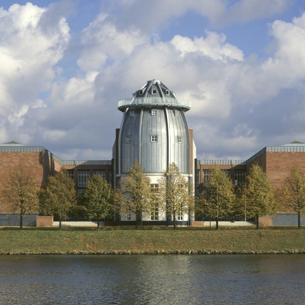 Een vergezicht van het Bonnefanten Museum in Maastricht, een metalen, eivormig gebouw aan de rivier.