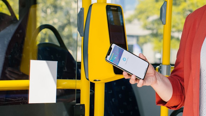 Een persoon checkt met de telefoon in bij een gele incheckpaal in een Arriva-bus.
