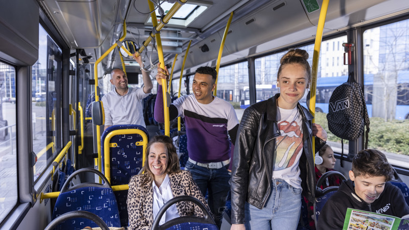 Meerdere reizigers die jong en hip gekleed zijn staan en zitten in een Arriva-bus en moeten lachen.