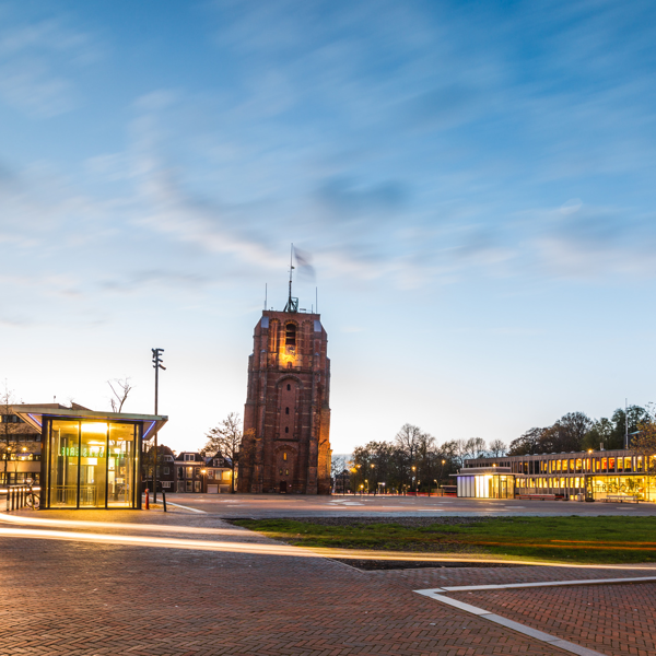 Het voorplein van station Leeuwarden net voordat de zon ondergaat, uit alle omringende gebouwen komt licht.