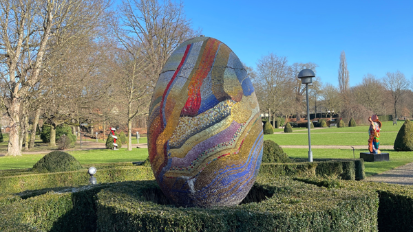 Een zeker drie meter hoog mozaieken en veelkleurig ei staat in een tuin.