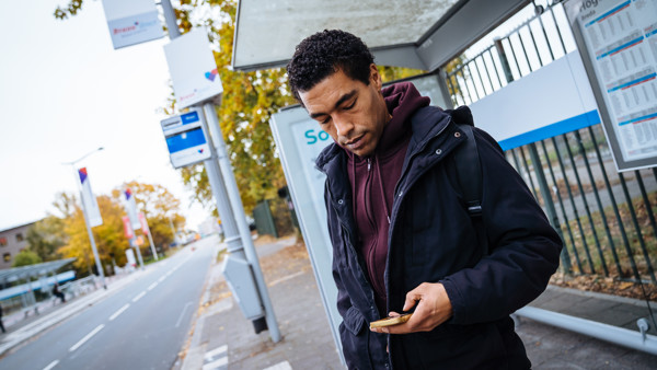 Een man staat bij een bushalte en kijkt op zijn telefoon. Een man staat bij een bushalte en kijkt op zijn telefoon.