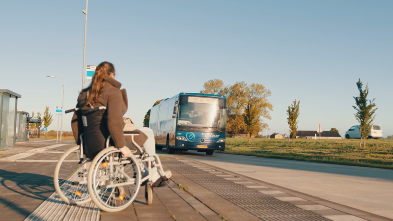 Reiziger in een rolstoel zit bij halte, bus komt aanrijden